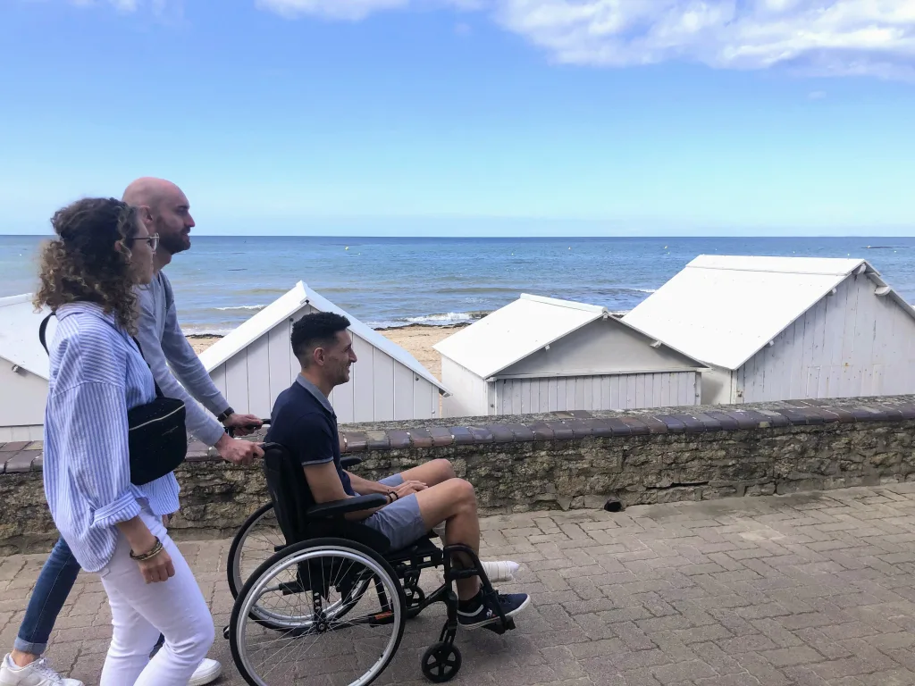 Balade en fauteuil roulant entre amis sur la digue promenade de Saint-Aubin-sur-Mer